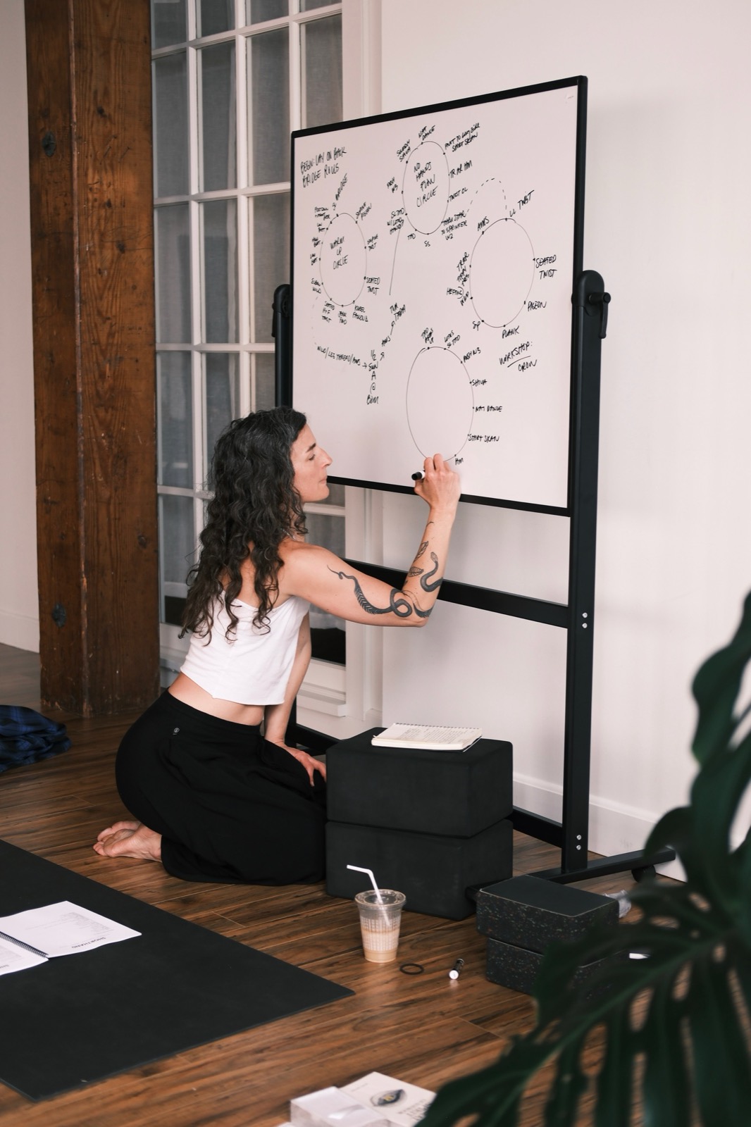 Bonnie Weeks kneeling at a whiteboard, drawing the circles of a class plan in marker